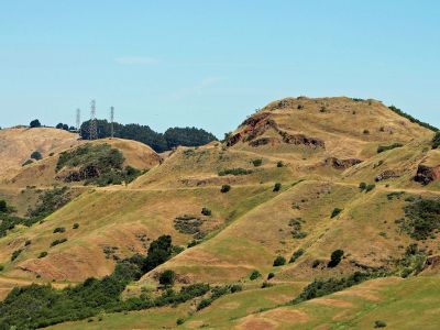 hillside of sibley volcanic preserve spotted with some darker green shrubs and some antennas on top of one hill